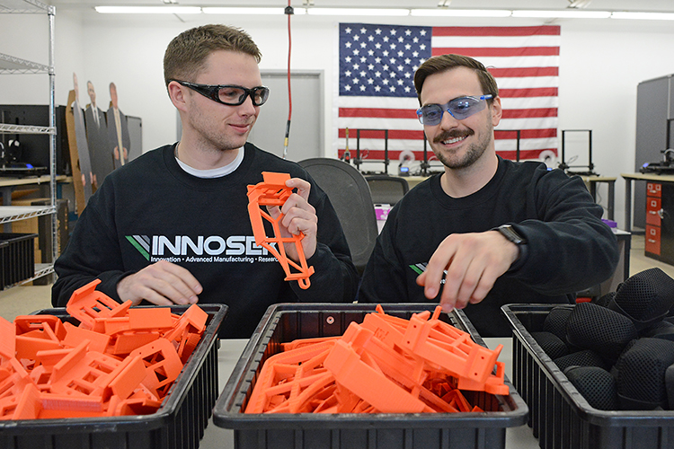 Brian Bischoff and John Kappel assemble cell phone cradles they produced for the automotive industry with 3D printers.