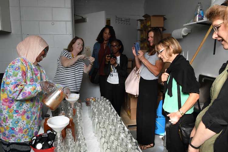 A group from United Way visiting Broadway Market watches as Bisharo Ali bottles some of her savory sauce.