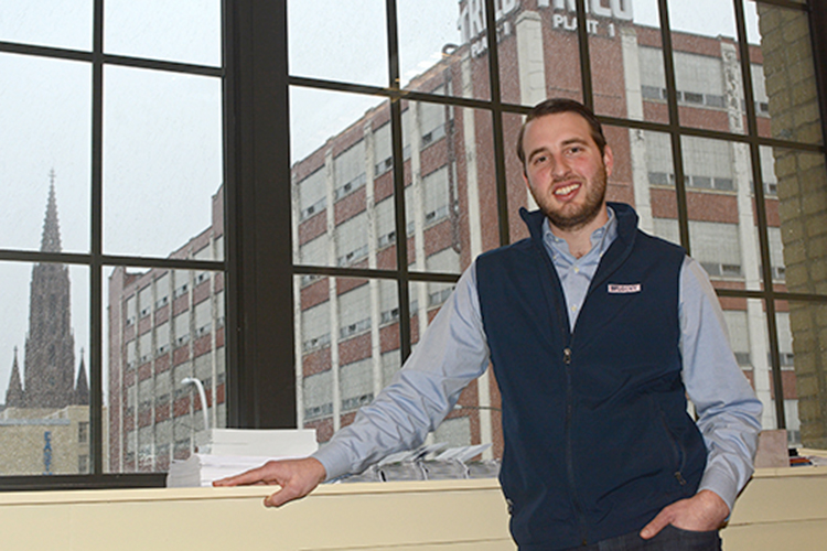 Framed by a signpost of Buffalo’s industrial past, the Trico Building, Alex Killian, associate with The Investor Network, stands in his Goodell Street office. 